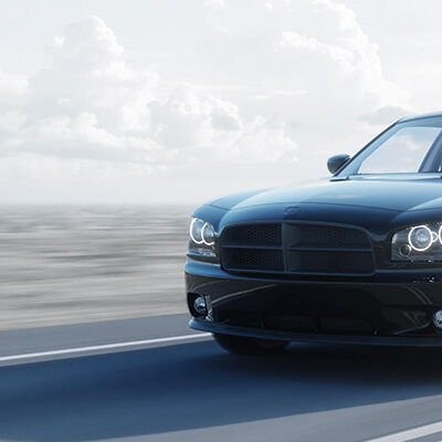 A black car driving down the road with clouds in the background.